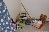 Photo showing a collection of sewing-related items including Singer model 4610 sewing machine, books, fabric, and patterns arranged on the floor with ironing board nearby