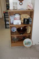Full view of wood shelving unit and contents including ice cream maker, salad bowl, decorative items and plates.