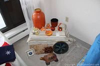 Full view of the lot including tall orange vase, Halloween ornaments, pottery plate, tile trivets, crackled glass bowl, and wooden turtle.