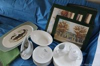 Full view of fish platter, white china plates including dinner and side plates, gravy boat with ladle, cream and sugar set, board style placemats with building prints, and woven placemats on blue background.