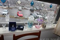 Photo showing Swarovski bear, pair of earrings in box, signed blown glass apple, clear glass vase with blue marbles inside, and smaller clear decorative items on windowsill.