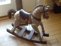 Gray wooden rocking horse with white polka dots, dark brown saddle, showing profile view on a wooden floor.