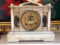 Front view of marble clock with brass Roman figures on either side of the clock face.