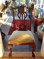 Front view of a wooden chair with carved openwork backrest and light-colored fabric cushion with tear on seat corner.