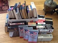 General view of boxed collection of books, VHS tapes with some visible titles such as 'Gandhi' and 7-Up branded videotapes.