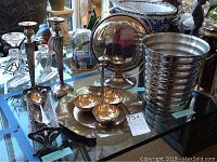 Table displaying the silverware including silver platter, condiment holder with bowls, wastebaskets, and decorative stand among other items.