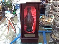 Front view of wooden display case containing the Coca Cola bottle with red satin backing.