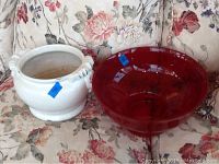 Photo showing white ceramic planter and large red glass bowl on floral couch