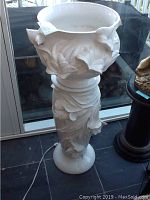 Full view of white ceramic planter on matching pedestal, showing floral design and shape