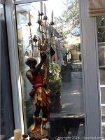 Frontal view of full statue figure holding candelabra against window background