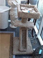 Full view of beige carpeted cat condo showing top cushioned square platform, middle platform, vertical post, and angled ladder.