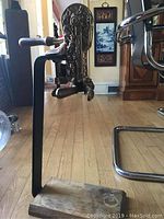 Side view of the standing metal wine cork stand showing detailed embossed mechanism and wooden base with stains.