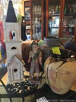 Photo showing all four items: two ceramic vases, wooden statue, and wooden church birdhouse standing on glass table.