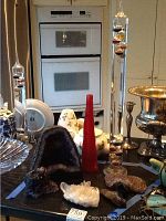 Overview of large amethyst geode, red vase, Galileo thermometer and assorted crystal specimens on table