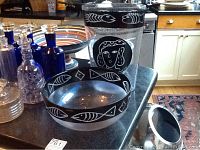 Two decorative glass pieces: a black and white crystal vase with abstract face and fish designs, and a Kosta Boda glass bowl with black and white fish motif band.