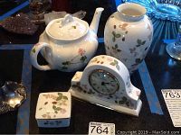 Overview showing four-piece set: teapot, vase, mantel clock, and trinket box with floral and berry patterns on bone china and porcelain surfaces.