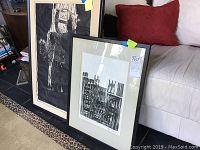 Two framed artworks leaning against a sofa on a leopard print rug. Smaller framed print in front is 'Quiet Harlem' signed by Cliff Harrison.