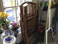 Two folded bamboo chairs leaning against window, one with taped broken cane backrest.