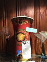 Front view of red porcelain vase with Medusa head motif flanked by glassware