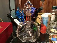 Full view of clear glass decanter with stopper on tabletop amid background items