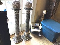 Two tall decorative posts covered in sea shells standing on a hardwood floor near a door. Both posts are about 38 inches tall with some missing shells evident on their surfaces.