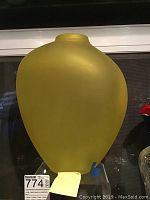 Frosted yellow glass vase displayed upright with rounded body and narrow neck, seen against a window background.
