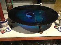 Blue glass plate displayed on a stand beside decorative items.