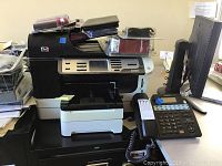 Photo showing HP OfficeJet Pro 8500 printer with several items on top and next to it including flashlights and other accessories.
