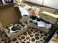 Three unorganized boxes containing a security camera, accessories, and packaging materials on carpet