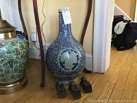 Full view of the blue and white ceramic vase with long neck and bulbous bottom, featuring ornate circular patterns and decorations with a tag attached.