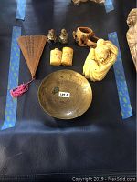 Full view of Asian collectible lot items on black surface, showing carved ivory figurine, brass dish, ceramic foo dogs, wood cup, carved ivory snuff bottles, and wooden fan.