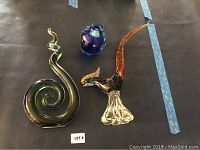 Full lot of three Murano glass pieces displayed on a surface, including a green spiral sculpture, blue vase, and bird figurine.
