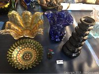 Top overview of all four carnival glass pieces including amber bowl, blue vase, black stacked vase, and round dish.