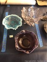 Three vintage glass bowls including a blue ruffled edge bowl, purple ruffled bowl, and pink leaf-shaped bowl.