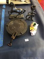 Top view of lot showing the cast iron bowl with lid, the horse figurine, ornamental piece, and ceramic figurine on a blue surface