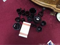 Multiple vintage Avon red glass pieces including bowls, vases, and candle holders displayed on red carpet with some items accompanied by original box.