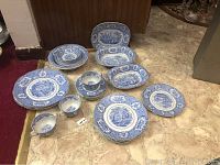 Photo showing assortment of blue and white oriental patterned dishes including plates, bowls, and cups arranged on floor.