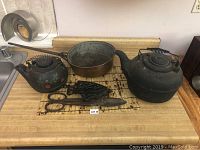 Full lot including copper pot, two cast iron kettles, large iron shears, and two ornate cast iron trivets on a kitchen counter.