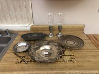 Full view of five silver plated serving pieces and pair of sterling silver weighted candlesticks with glass globes on countertop