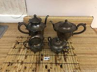 Four-piece silver plate tea set including two teapots, creamer, and sugar bowl on a bamboo mat on a counter.