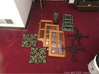 Overview of all items on burgundy carpet showing three wood glass cabinet faces, two decorative metal wall pieces, two black metal crosses, three small metal wall pieces, and a tall oval art glass vase.