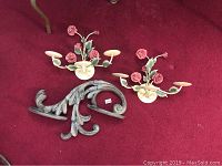 Photo showing two vintage Towle-style floral metal candle holders and one decorative wooden wall shelf with carved leaf scroll design, arranged on red carpet