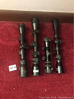 Four rifle scopes placed on red carpet. From left to right: CenterPoint 3-9x32, Bushnell waterproof 3-9x40, Tasco 3-9x32, and 4x28 scope. All scopes have black metal finish with mounting rings attached.