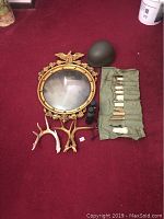 Full lot overview showing all items on red carpet including mirror, helmet, antlers, knife set, and binoculars.