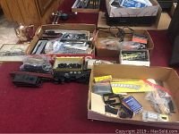 Top-down view of several open boxes containing assorted model train parts and accessories including wheels, track connectors, and pieces.