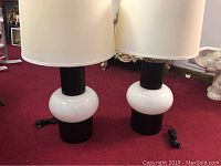 Pair of contemporary table lamps on carpeted floor, black base with white spherical section, white fabric shade.