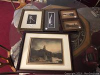 Framed vintage artworks laid out on a round table; includes multiple framed paintings and prints of birds and landscapes.