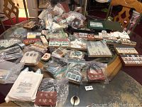 Large assortment of wooden collectible houses spread across a table, bagged and loose, showing variety in style and color.
