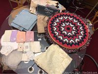 Overall assortment of vintage textiles displayed on glass table including folded linens, quilted round topper, crocheted piece, doilies, and napkins.