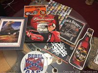 Photo showing framed eagle print, Harley-Davidson sign, Budweiser poster with driver and race car, Jack Daniel's poster, Wicked Ale bottle-shaped sign, and Harley-Davidson graphic poster partially visible under glass table.